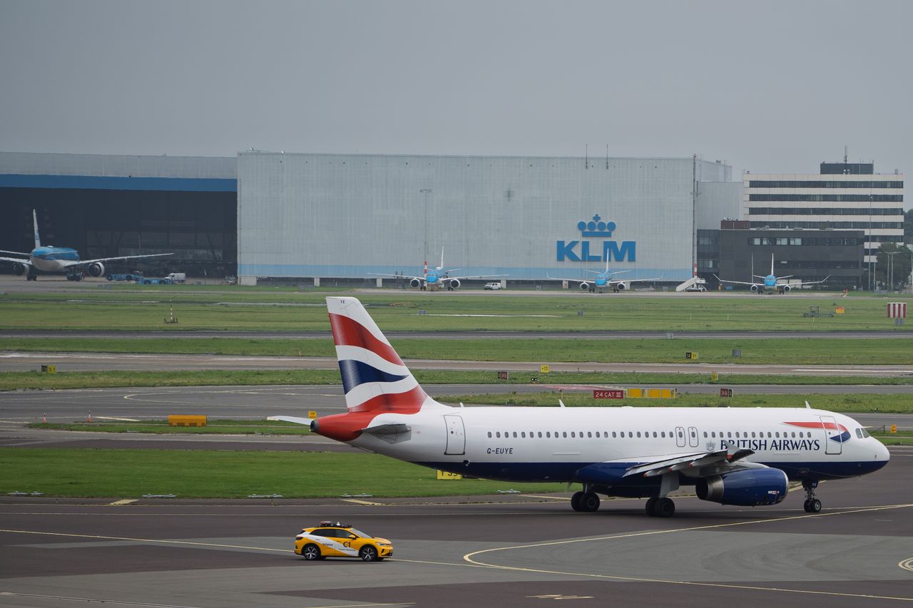 A British Airways aircraft taxiing at Amsterdam Airport Schiphol with a KLM hangar in the background.
