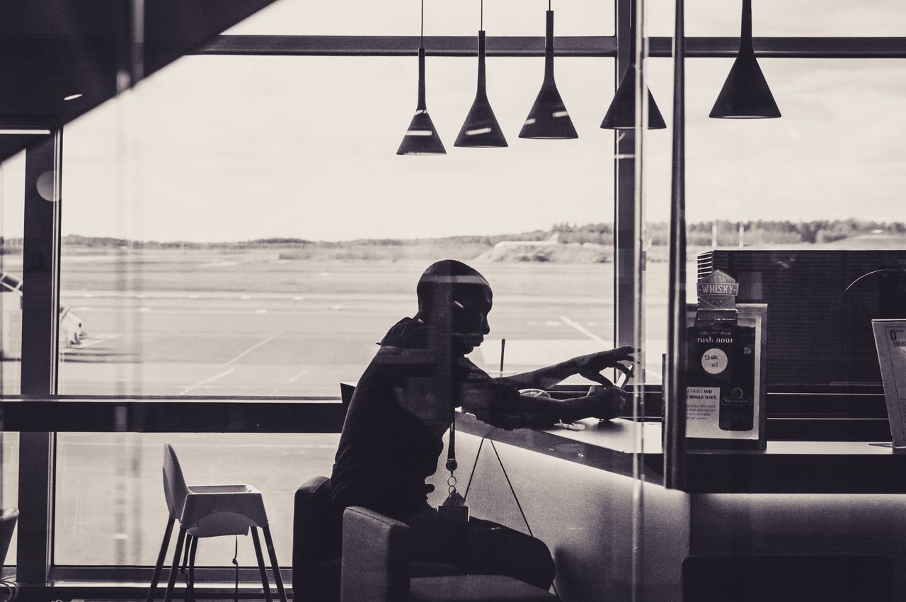 A black and white silhouette of a person sitting in an airport lounge, overlooking the runway.