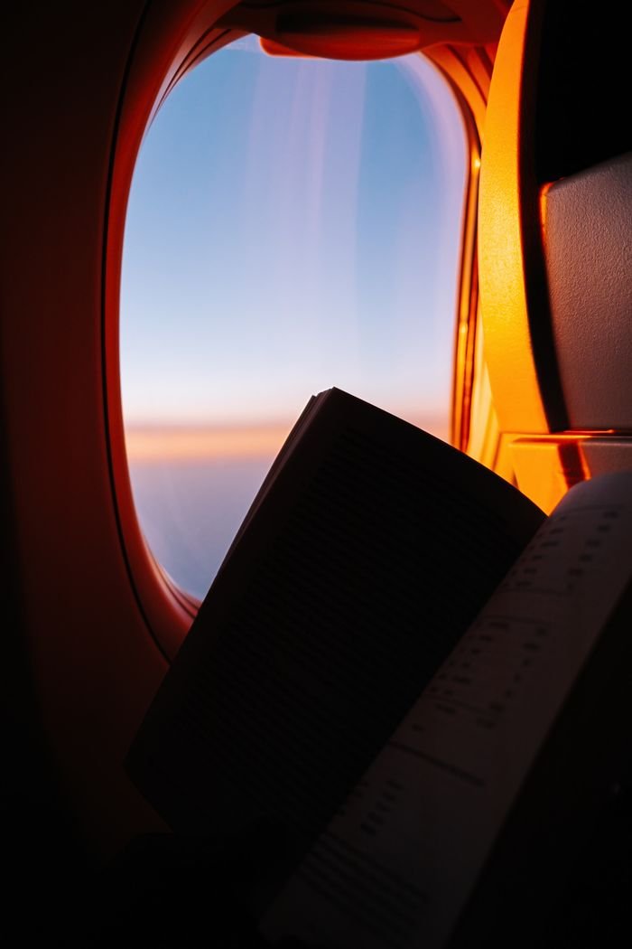 services-03 A serene moment of reading a book by an airplane window with sunset hues.