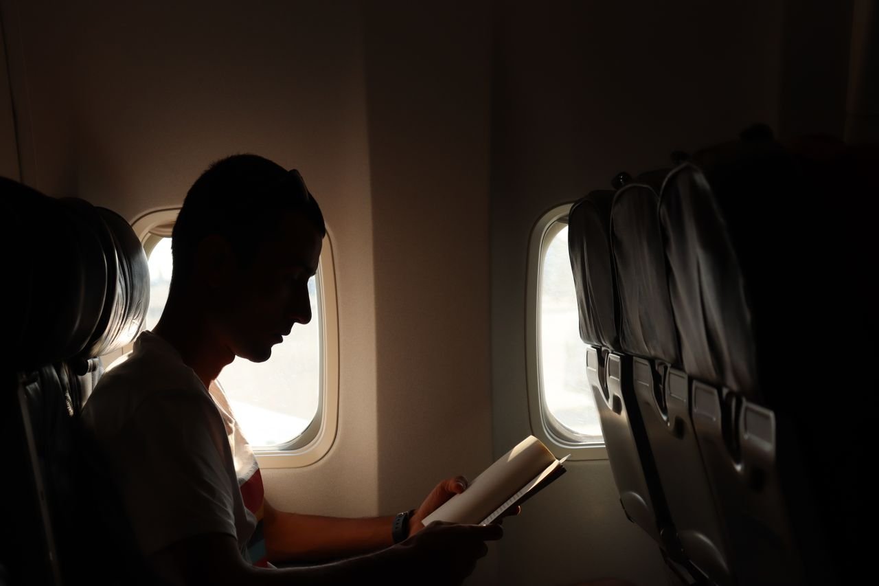 about-us-01 A man reading a book by the window, captured in a silhouette during flight.