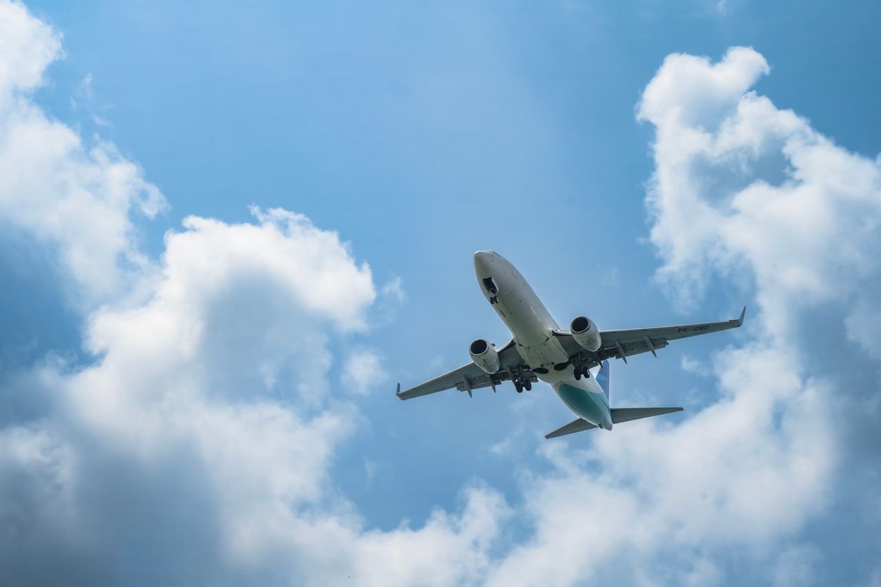 services-04 A commercial airplane soars in the sky with white clouds and blue backdrop, ideal for travel concepts.
